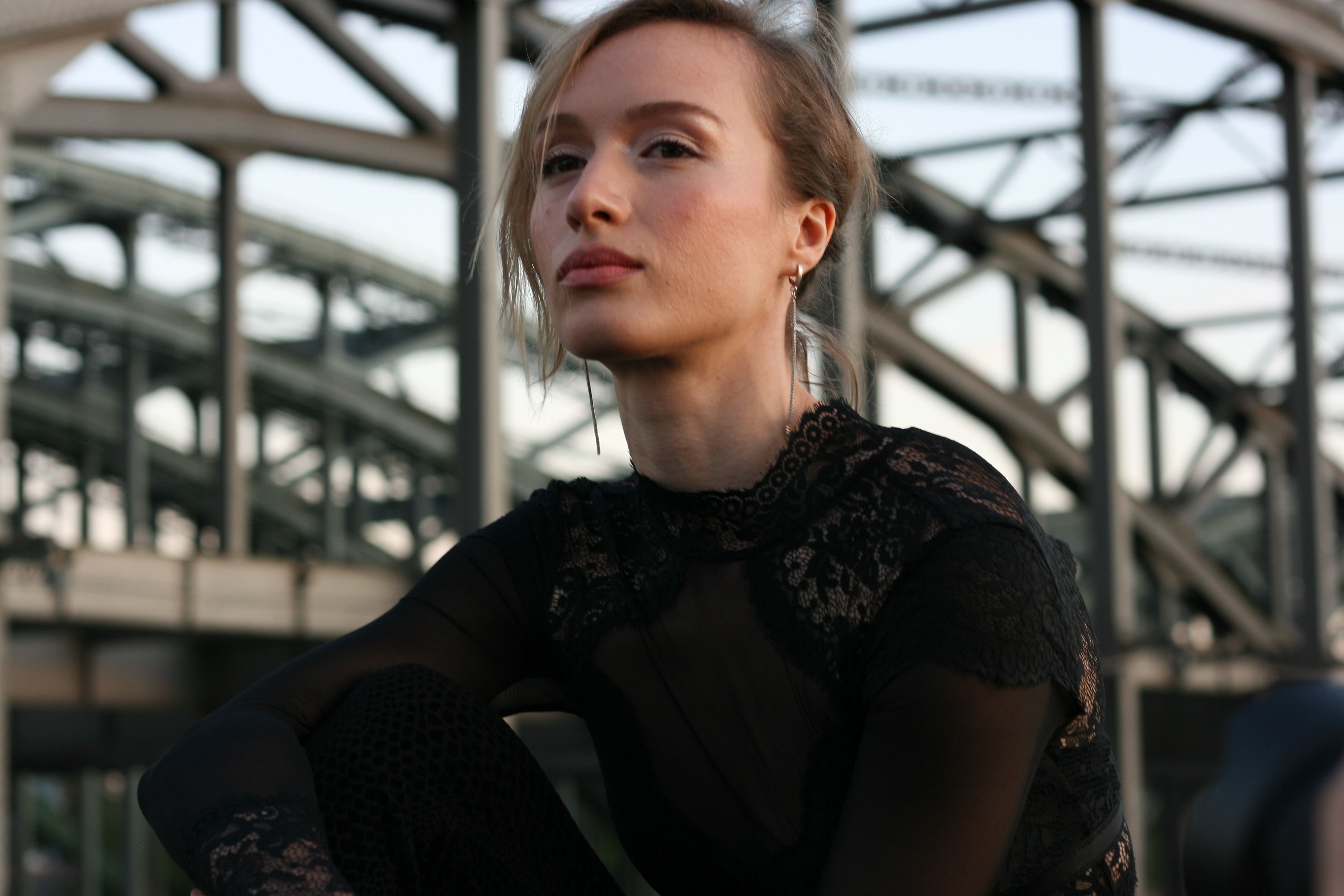 A woman in lace attire poses confidently against an industrial backdrop.