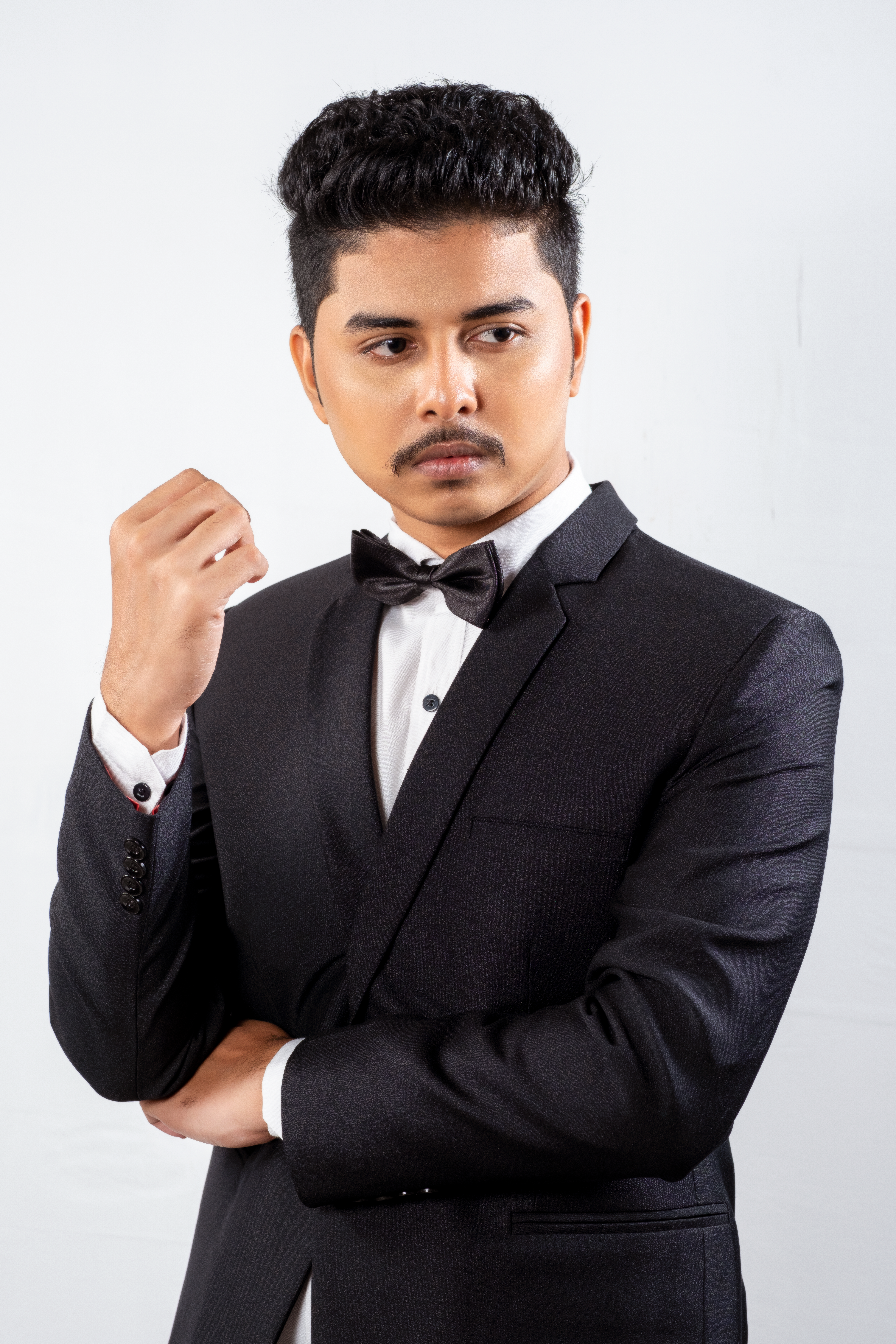 Stylish portrait of a man in a black suit with bow tie on a white background.