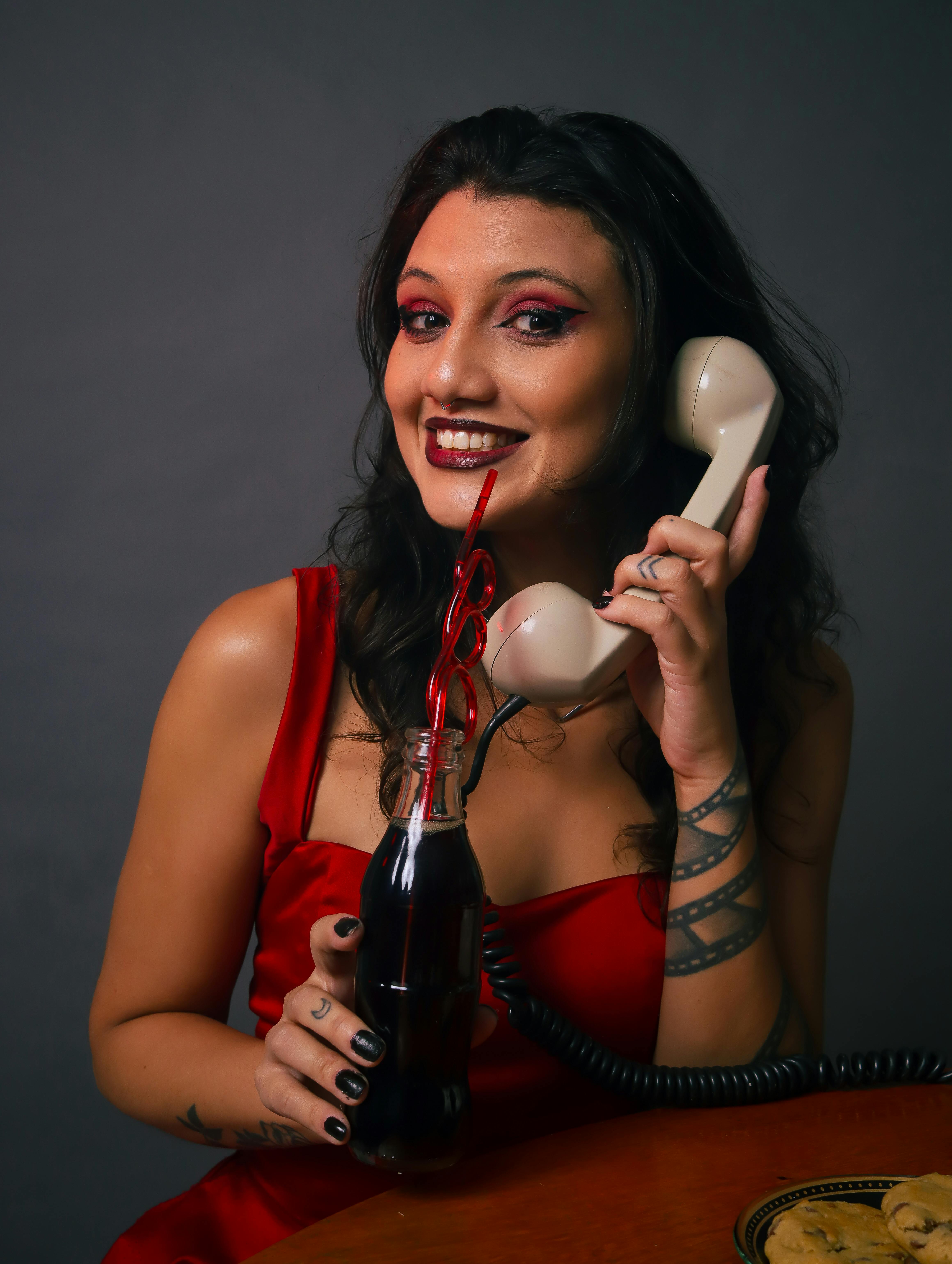 Woman in red dress holding a vintage phone and soda with heart straw.