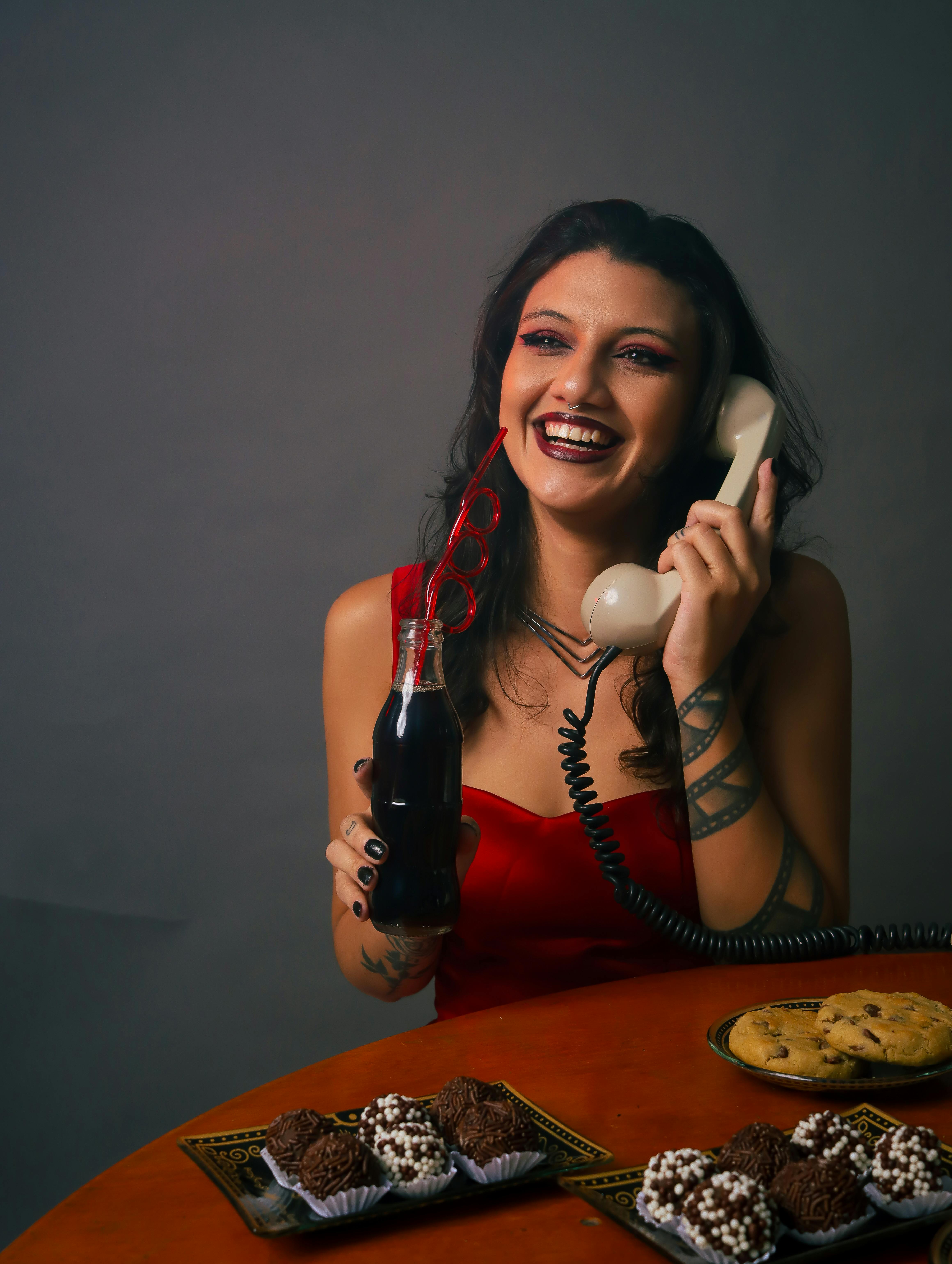 Miễn phí Người phụ nữ mặc váy đỏ cầm điện thoại cổ điển, đang thưởng thức đồ uống và đồ ngọt. Ảnh lưu trữ