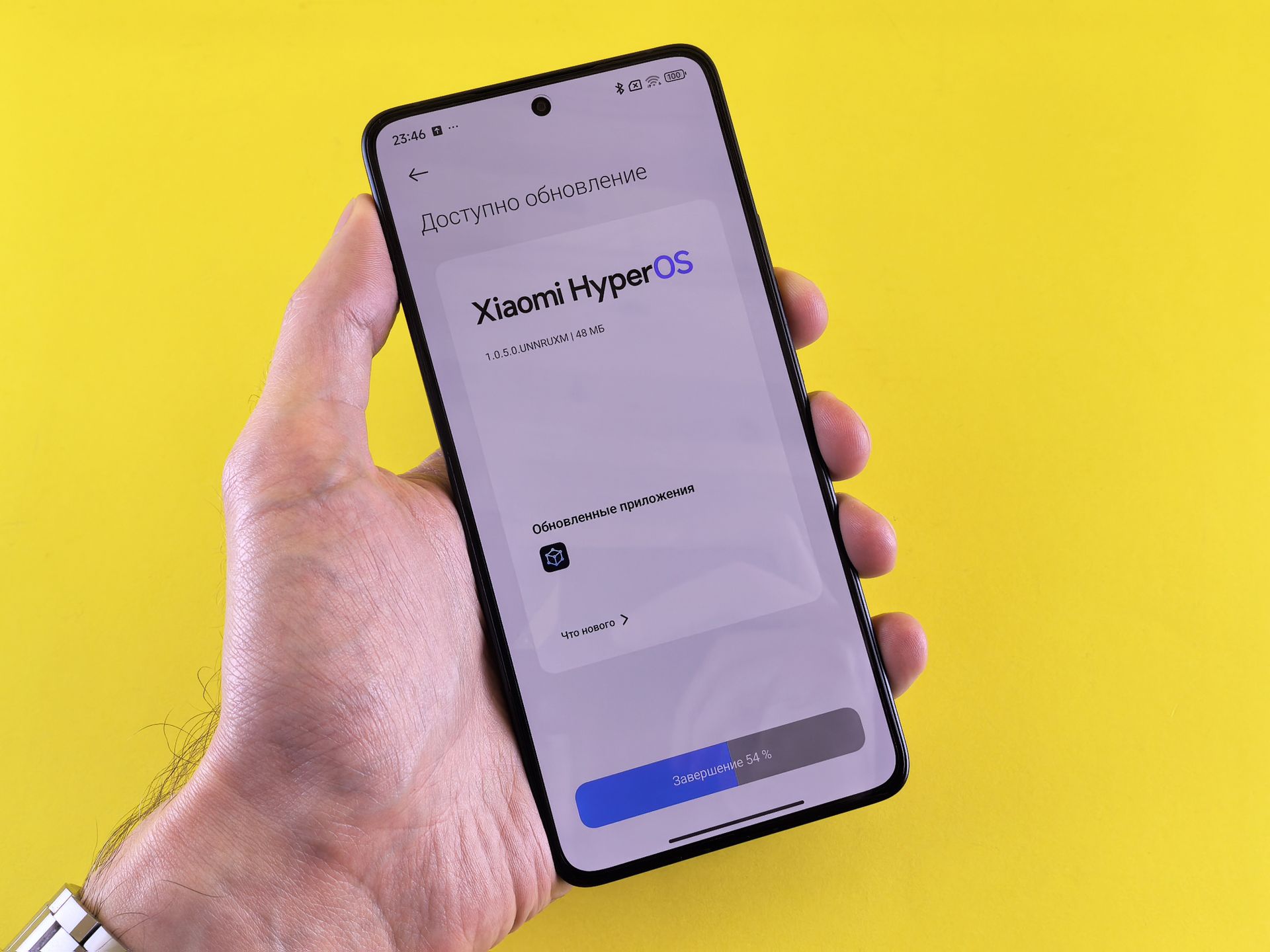 Close-up of a hand holding a smartphone displaying Xiaomi HyperOS update screen on a yellow background.