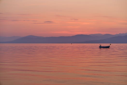 Tranquil sunrise over the calm sea in Corfu, Greece, featuring a small boat.