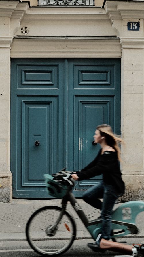 Free Blurry woman on bike passes a grand blue door, blending urban movement and architecture. Stock Photo