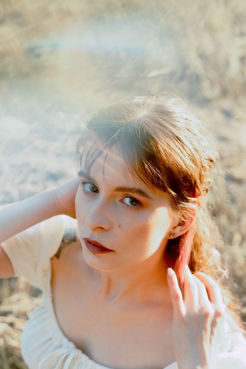 Free Beautiful portrait of a young woman in a sunlit field capturing an ethereal summer vibe. Stock Photo