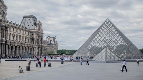 Free The Louvre Museum's iconic glass pyramid entrance in Paris, bustling with visitors. Stock Photo