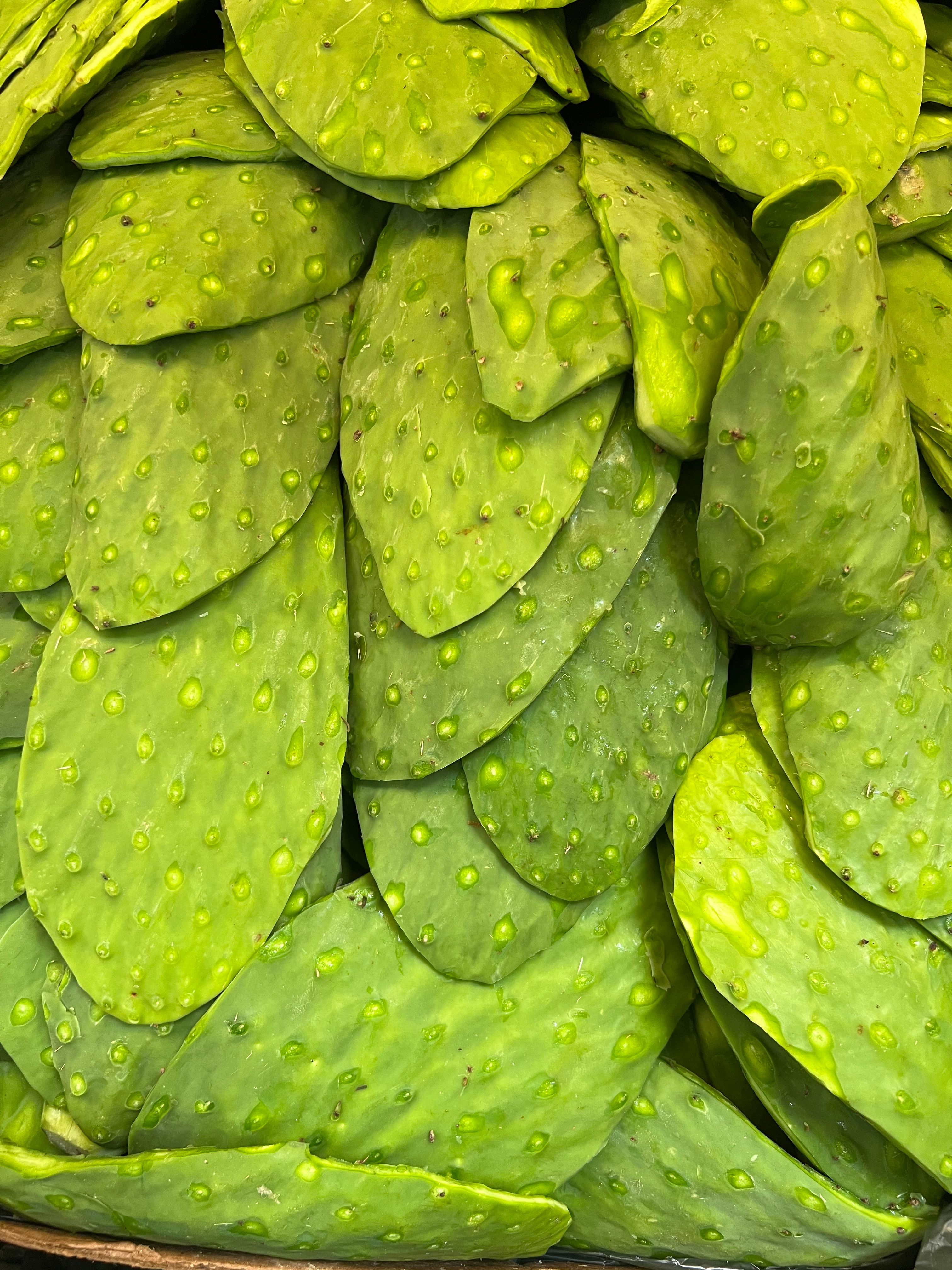 Trimmed green nopales paddles with the spines and edges removed, sliced into strips on a cutting board next to a whole uncut paddle.