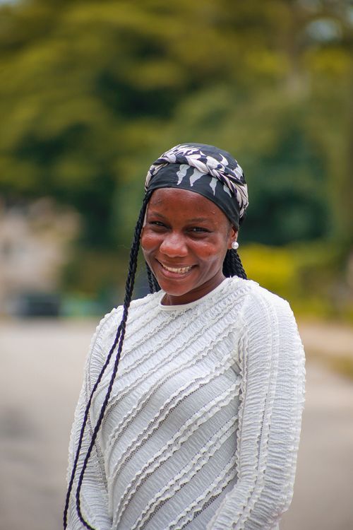Free Portrait of a smiling woman in a white textured sweater, outdoors on a sunny day. Stock Photo