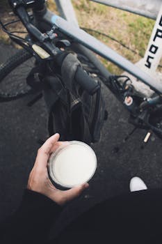 Close-up of a cyclist holding a cup of milk next to a bicycle outdoors.