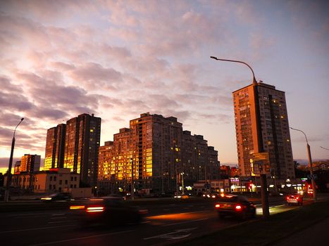 High-rise buildings glowing in sunset light, with moving cars on the street below.