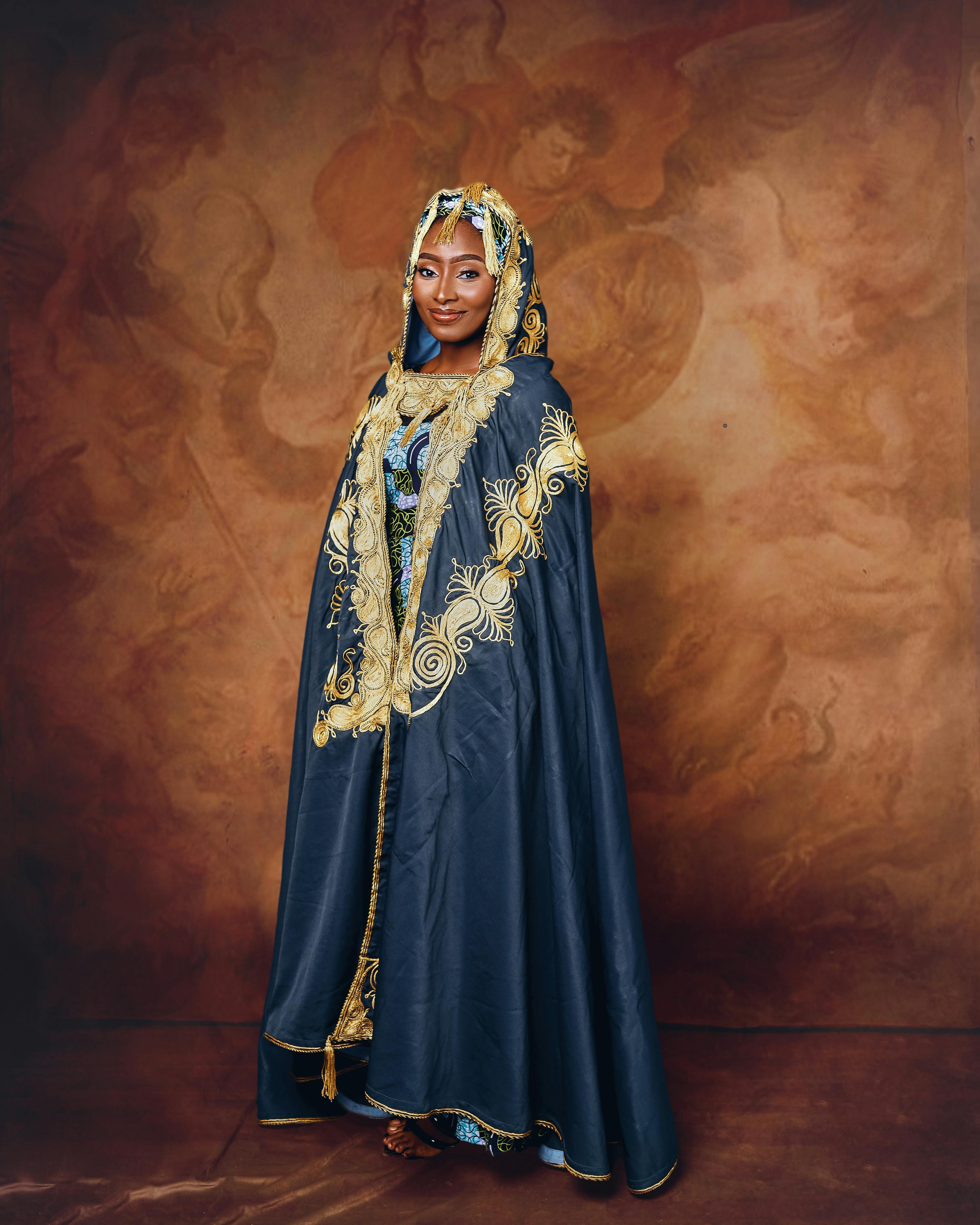 Woman in ornate traditional dress stands against a classic backdrop.