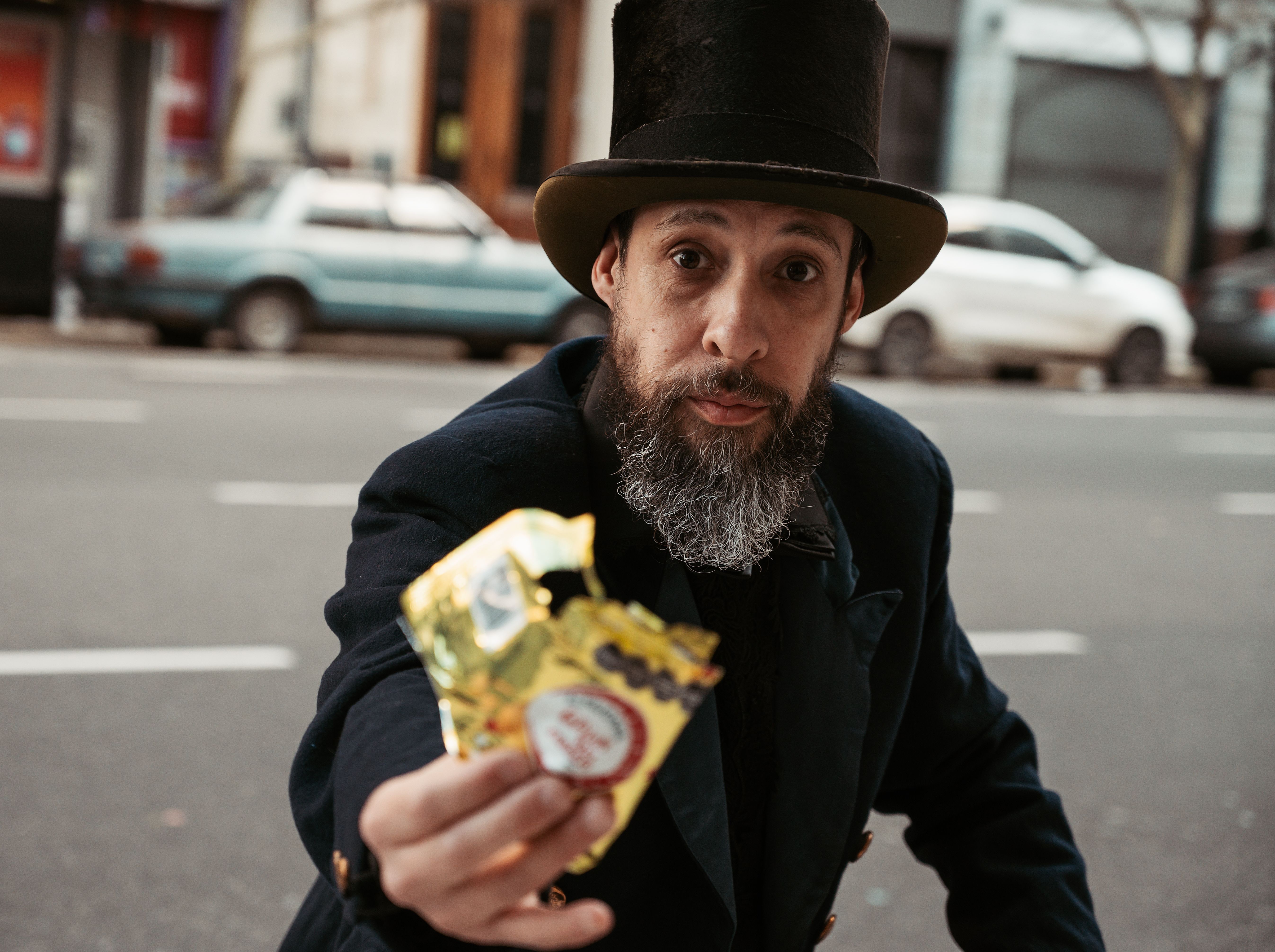 A man with a beard and a top hat offers a wrapped candy on a street in Buenos Aires.