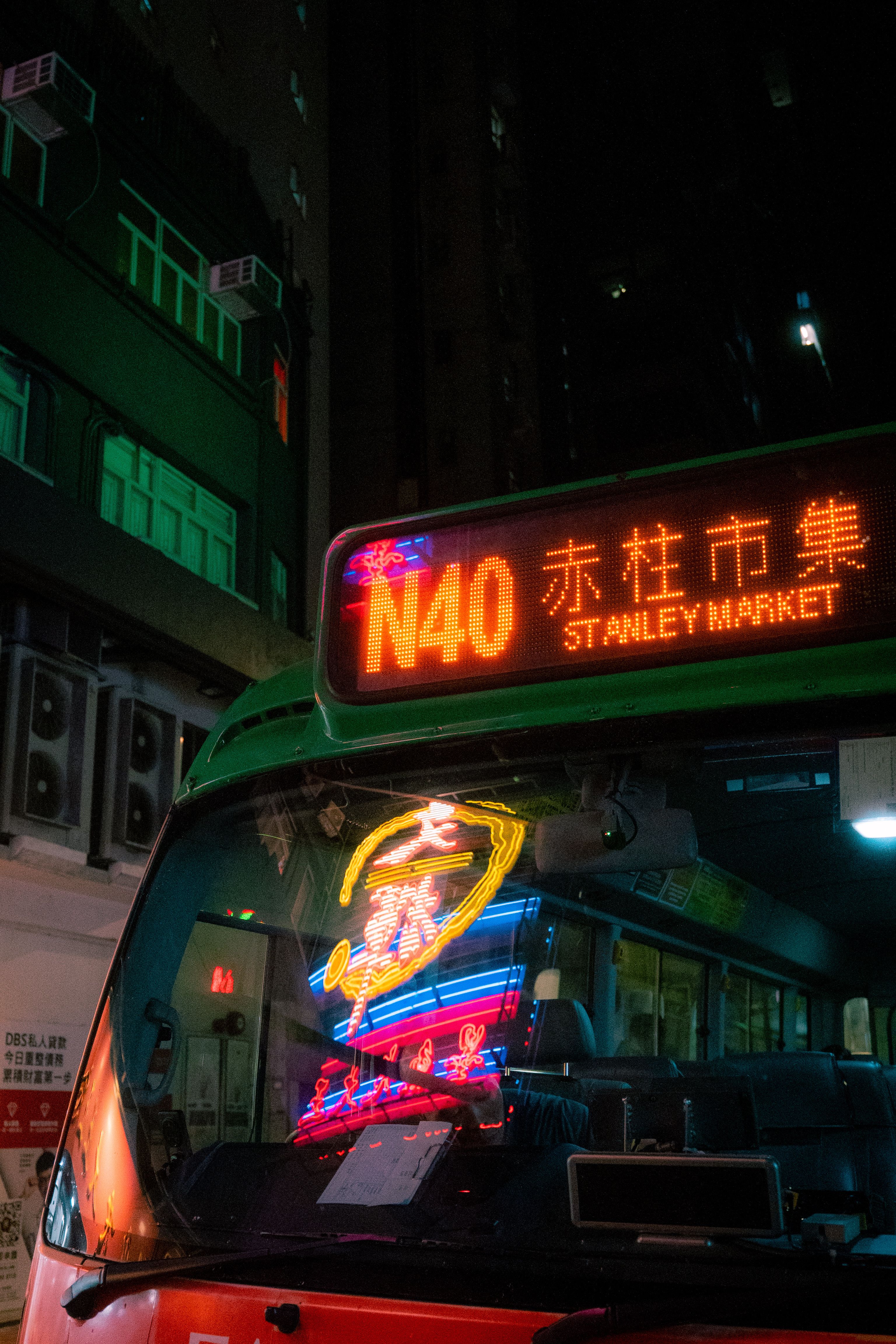 A vibrant night scene of a bus heading towards Stanley Market, illuminated by neon lights.