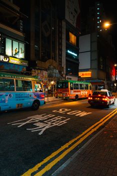 Brightly lit urban Hong Kong street with buses and taxis at night. Colorful and bustling.