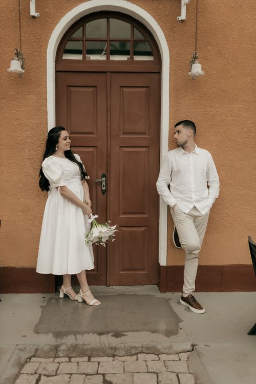 Free Elegant couple standing by a wooden door, wearing stylish outfits, creating a romantic ambiance. Stock Photo