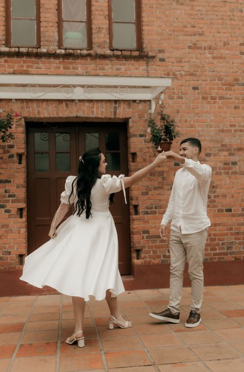 Free Happy couple dancing in front of a charming brick building, enjoying a sunny day together. Stock Photo