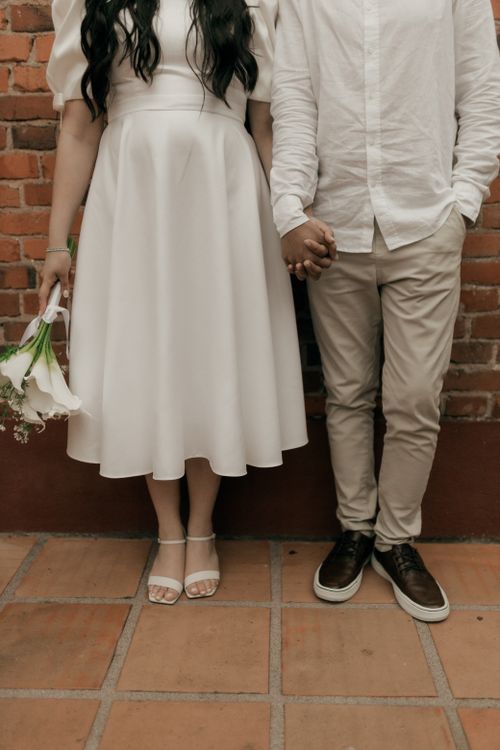 Free A couple in casual wedding attire holding hands against a brick wall. Stock Photo