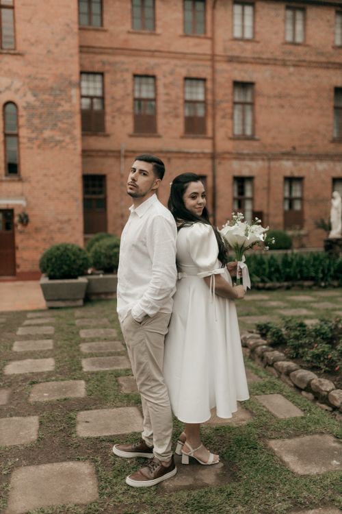Free Couple in elegant attire posing outdoors against a rustic building backdrop. Stock Photo