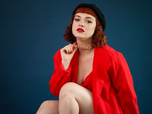 Free Woman posing in red jacket and beret against blue backdrop. Stock Photo