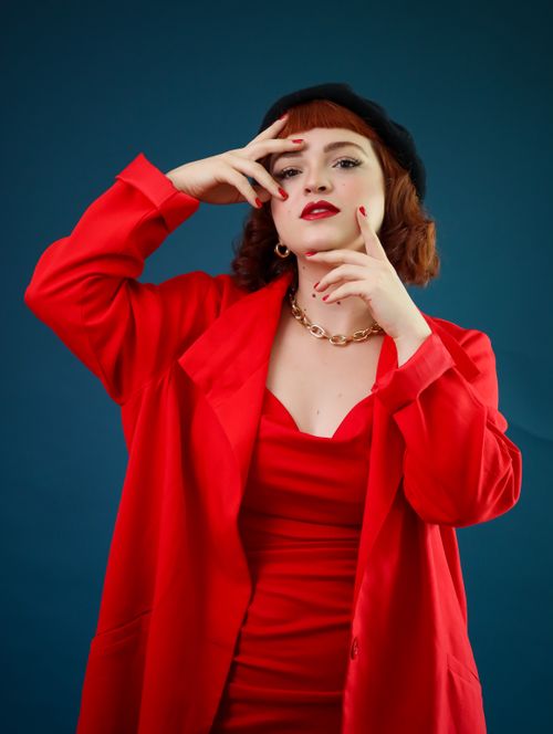 Free Stylish woman posing in red attire with blue background, exuding elegance and confidence. Stock Photo