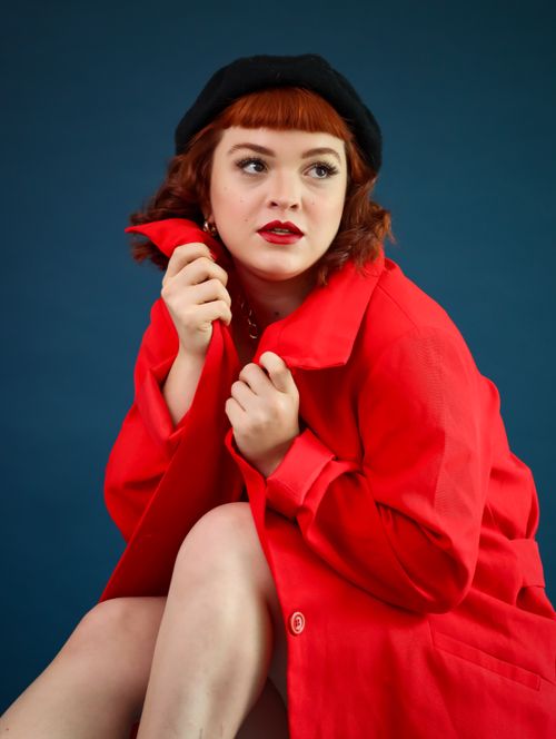 Free Stylish woman in a red coat and black beret against a blue background. Fashion portrait. Stock Photo