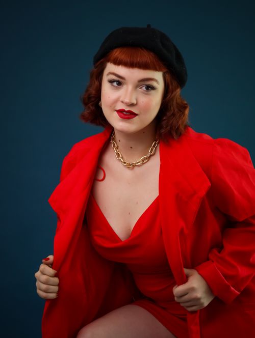 Free Portrait of a stylish woman wearing a red outfit, gold chain, and black beret. Stock Photo
