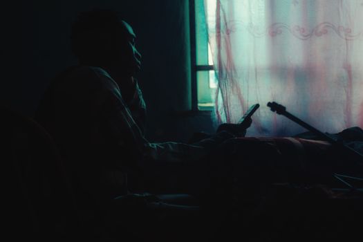 Silhouette of a person indoors, sitting by a window with a phone and guitar.