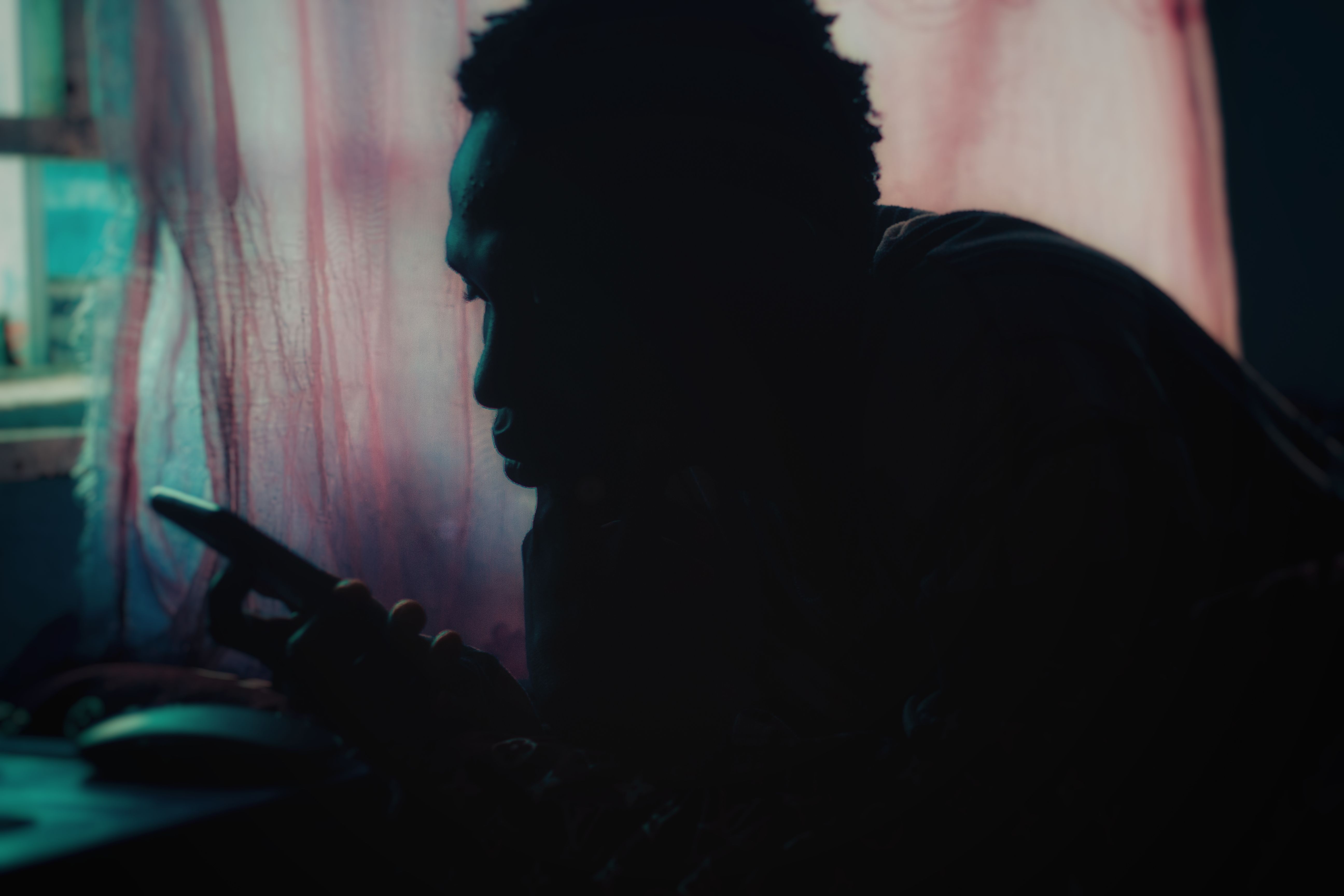 Silhouette of an adult using a smartphone near a window with soft lighting and moody ambiance.