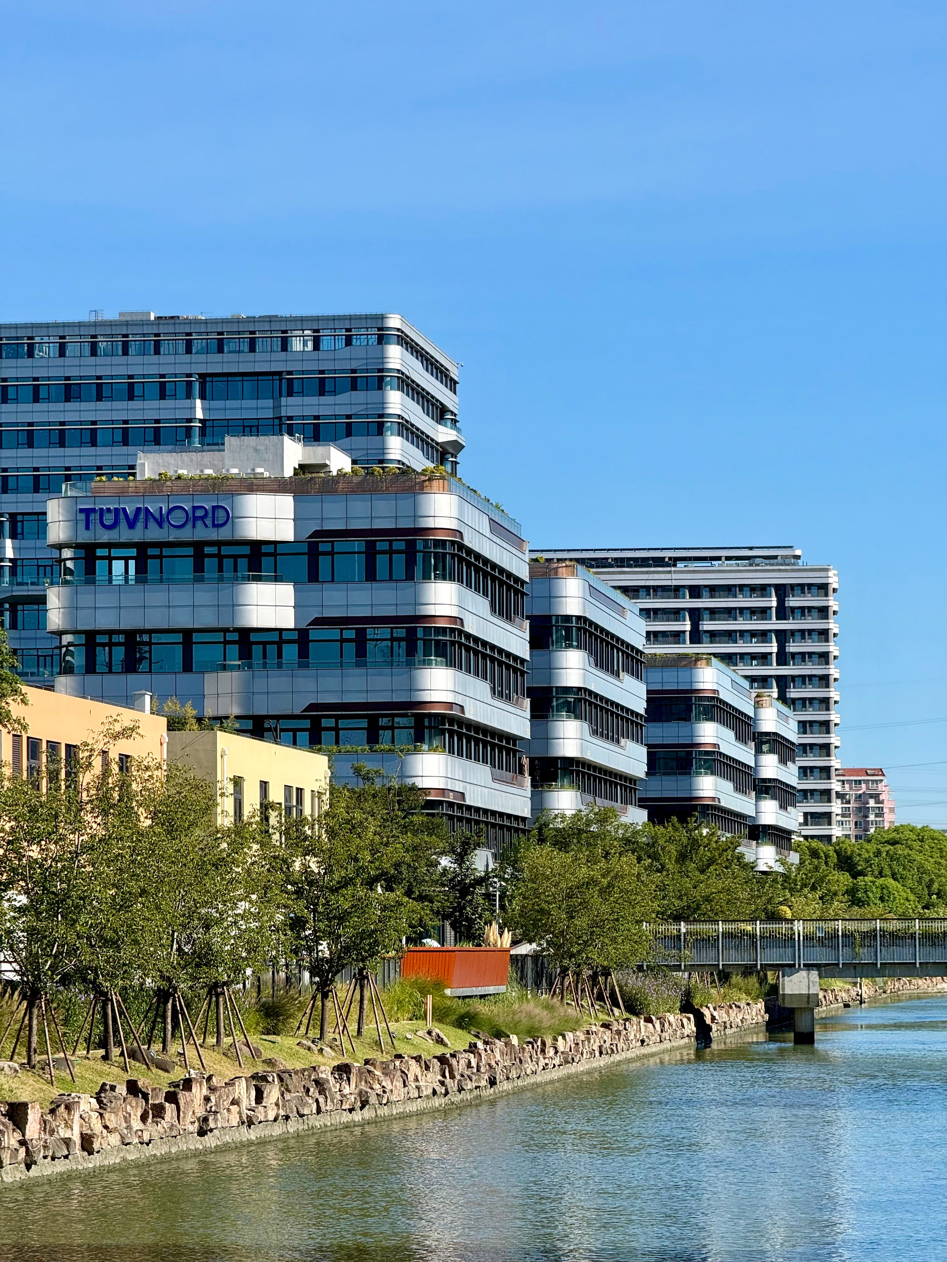 Contemporary office buildings by a canal under a clear, blue sky in Shanghai, China.