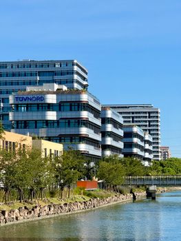 Contemporary office buildings by a canal under a clear, blue sky in Shanghai, China.