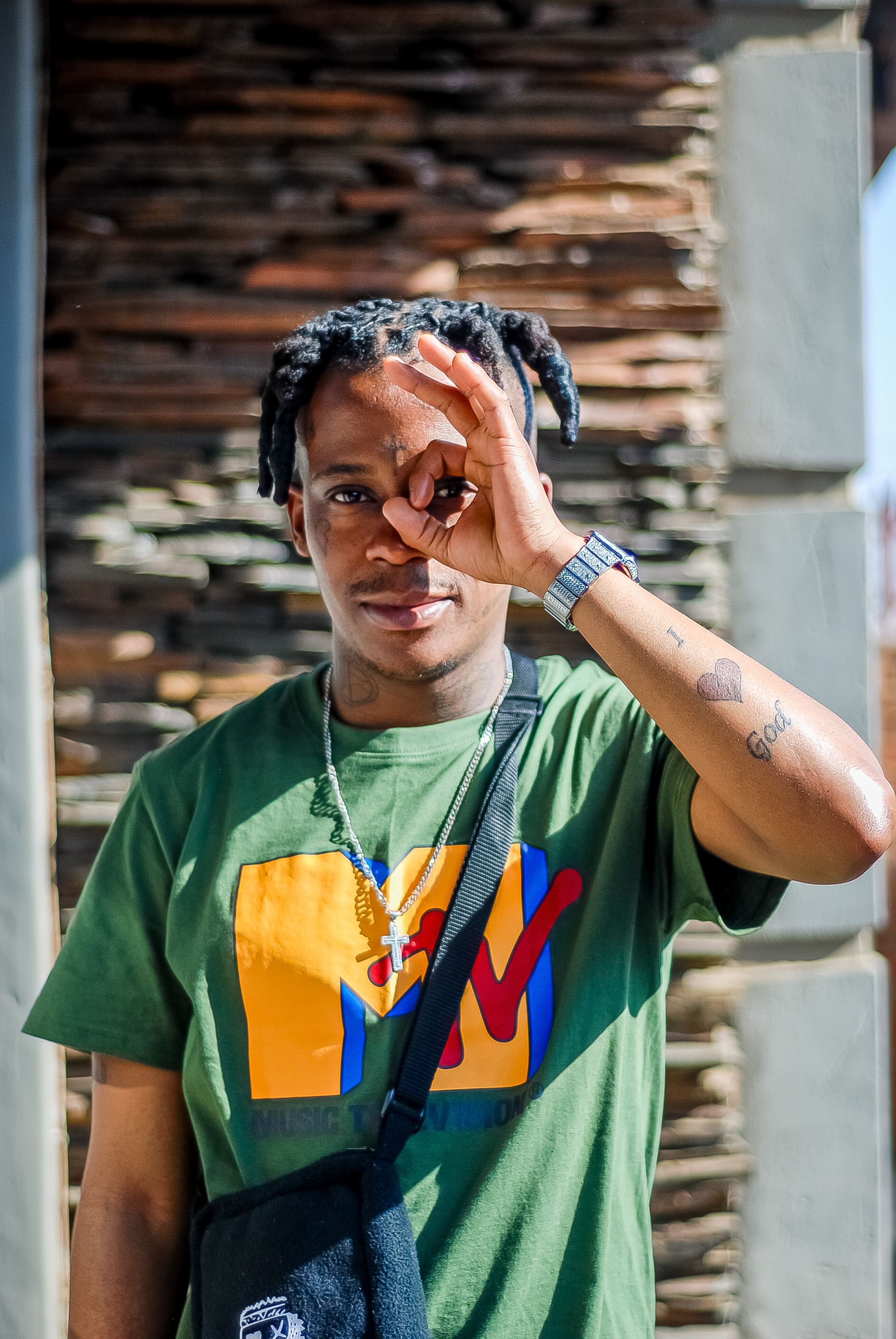 Young man with braids making an OK gesture outdoors on a sunny day.