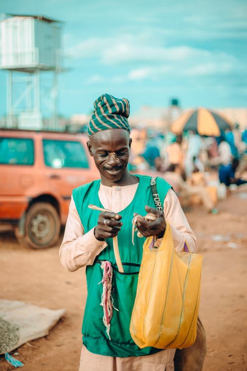 Free African market vendor in traditional attire, holding yellow bag, smiling. Stock Photo