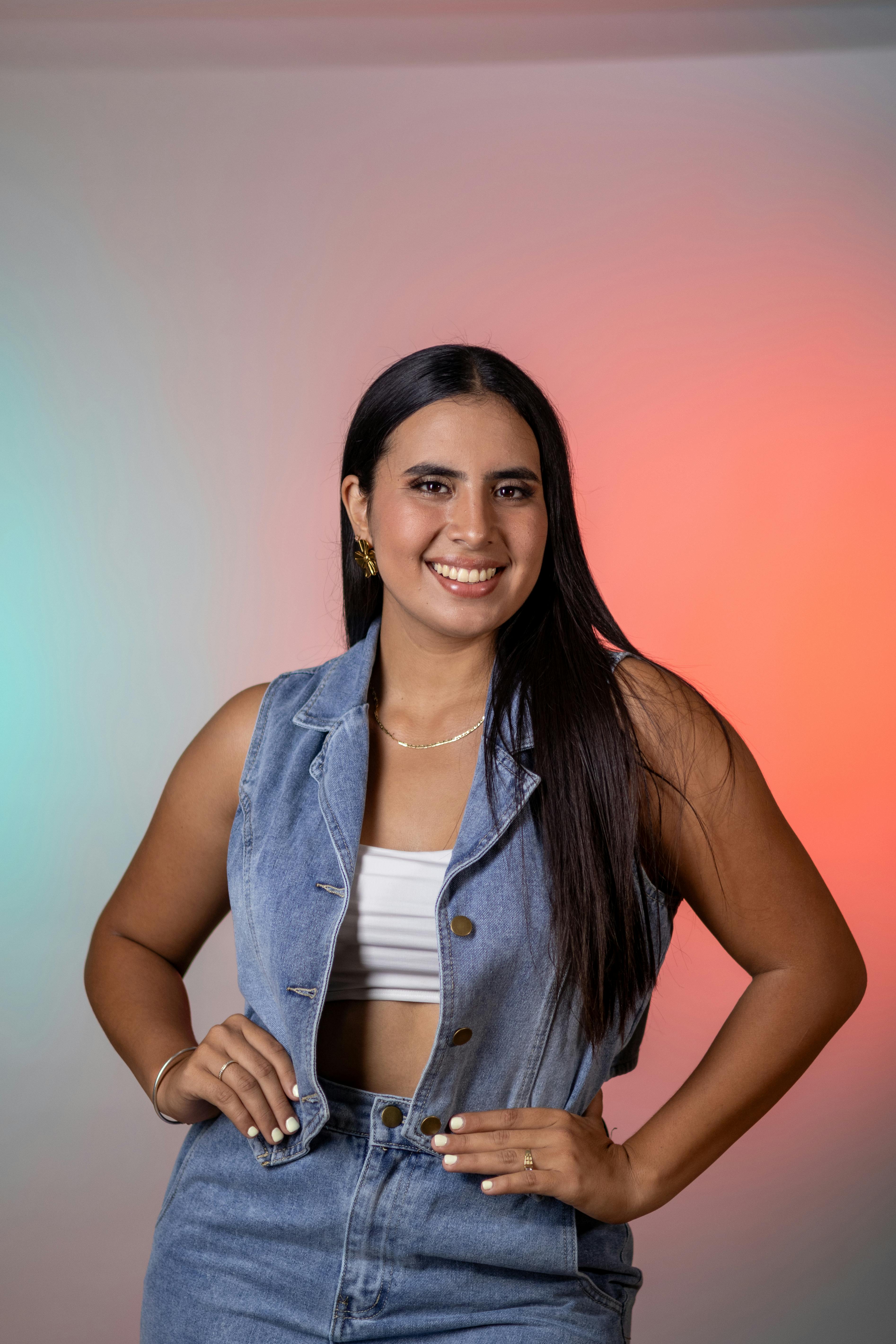 Confident woman smiling in denim vest, set against a vibrant gradient background.