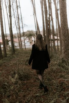 Back view of a woman walking through a serene forest path with tall trees and lush greenery.