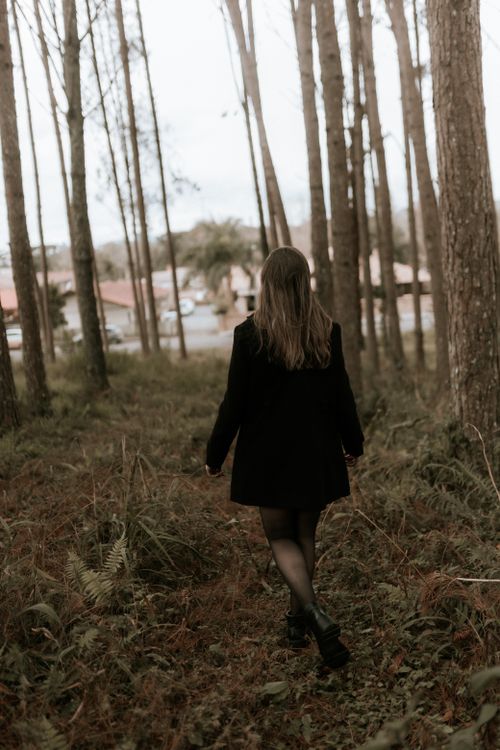 Free Back view of a woman walking through a serene forest path with tall trees and lush greenery. Stock Photo