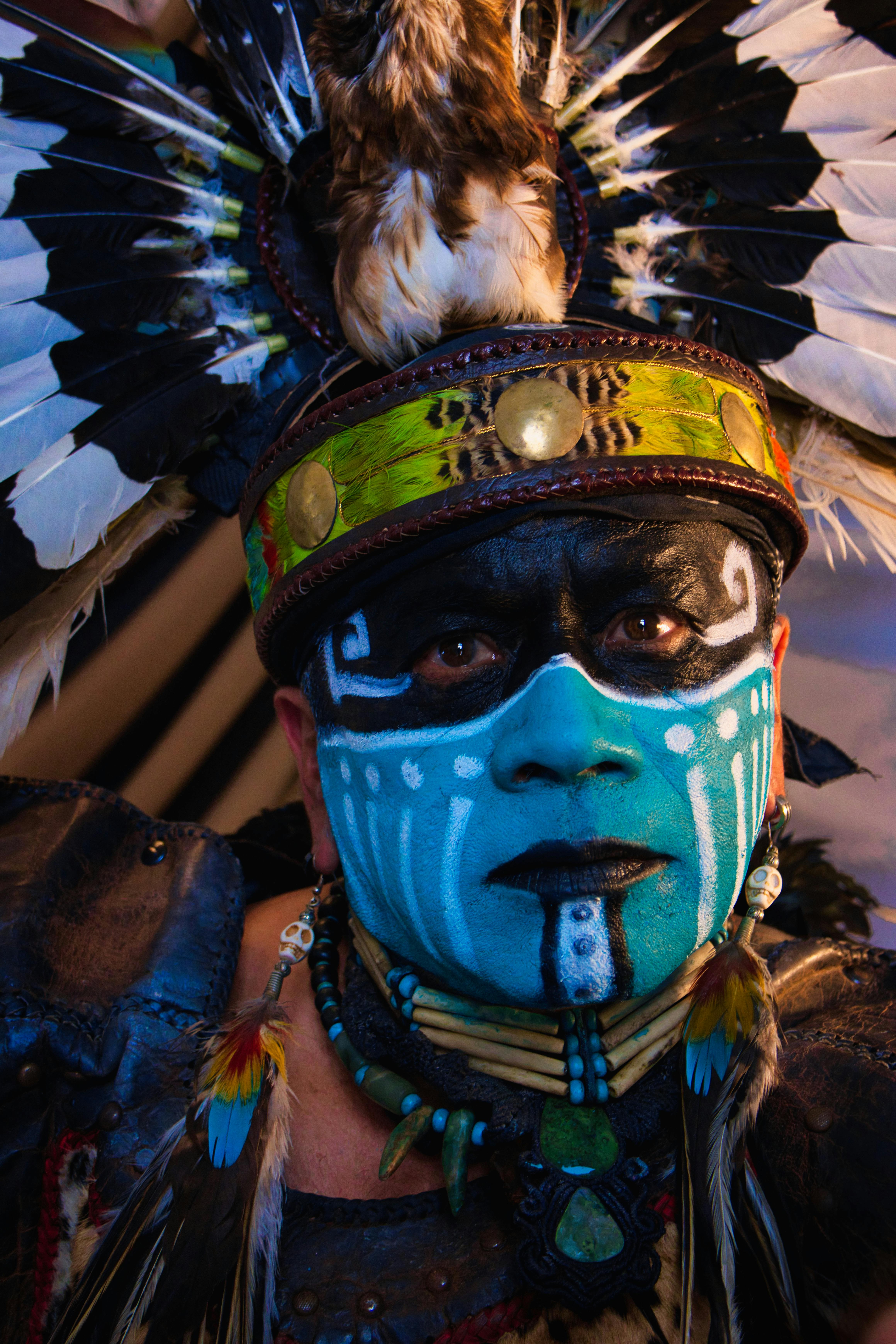 Close-up of a masked individual in traditional attire with feathered headdress and face paint.