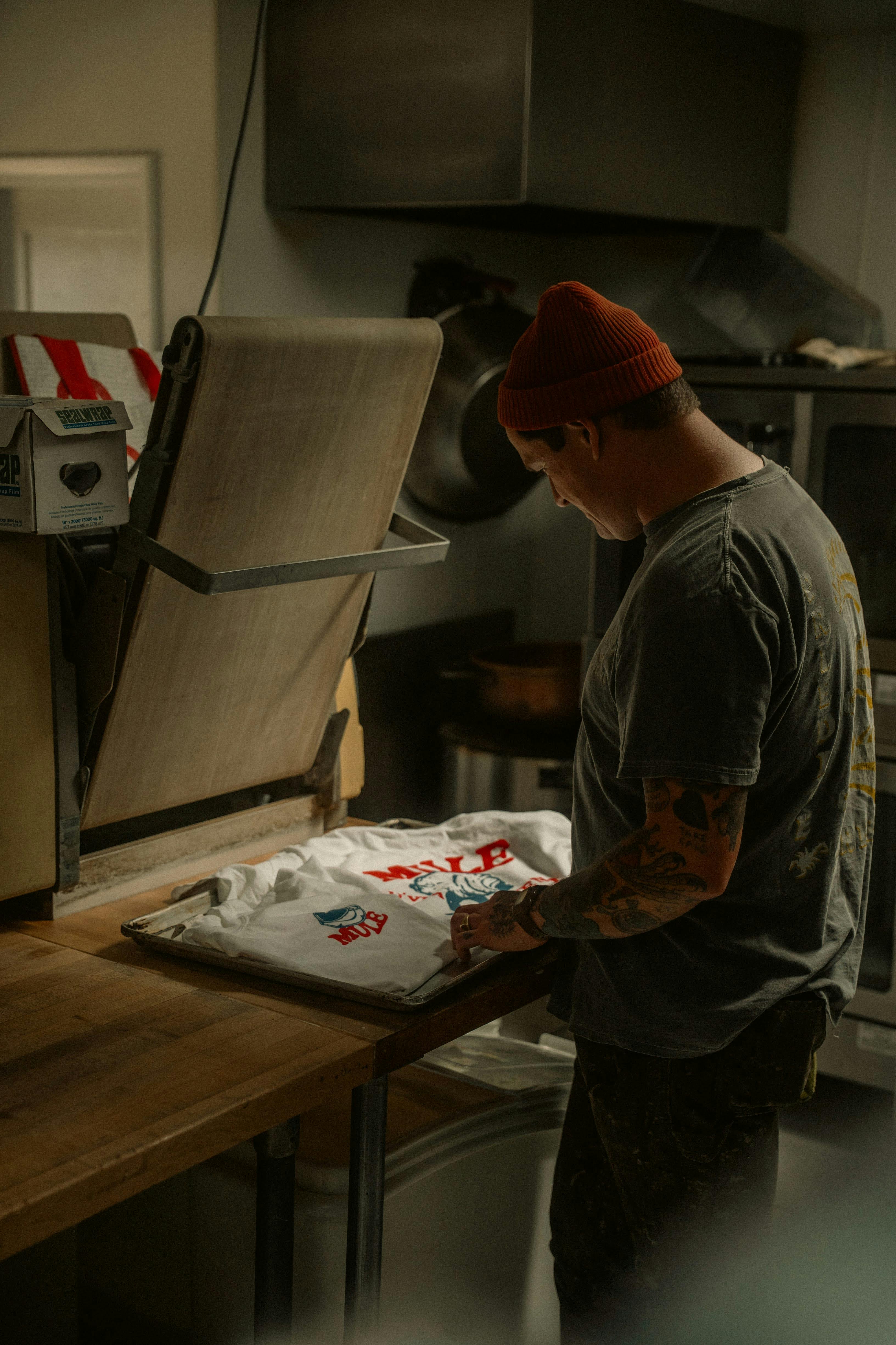 Man working on custom T-shirt printing in a dimly lit workshop.