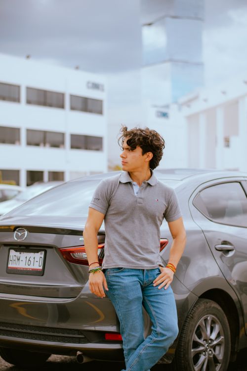 Free A young man in casual attire leaning against a car outdoors, exuding confidence. Stock Photo