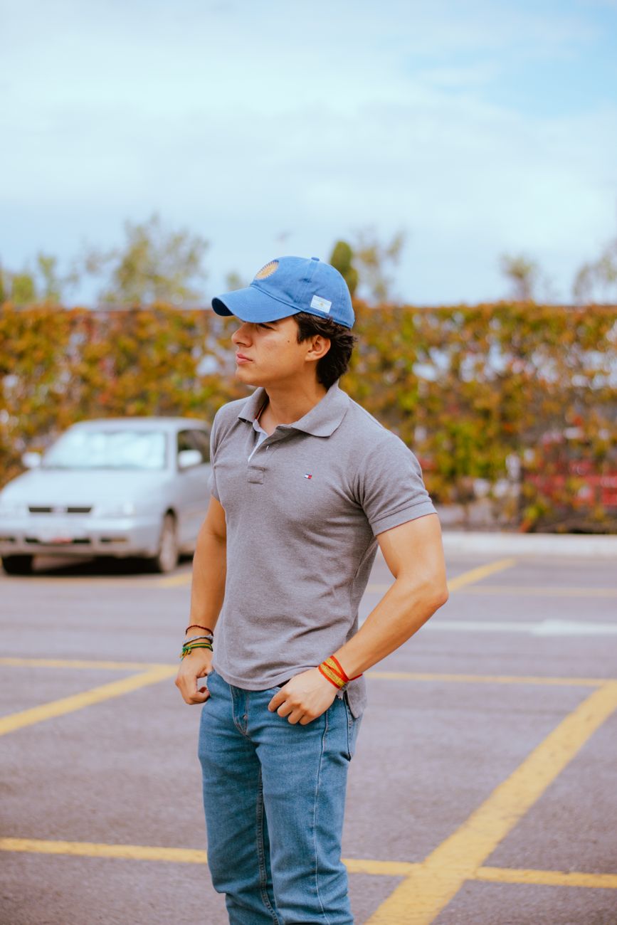 Casually dressed young man wearing a cap standing in an outdoor parking lot.