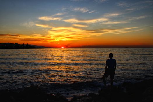 A serene silhouette of a person gazing at the sunset over a tranquil ocean.