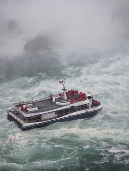 Tourist boat with passengers in red ponchos navigating the misty waters of Niagara Falls.
