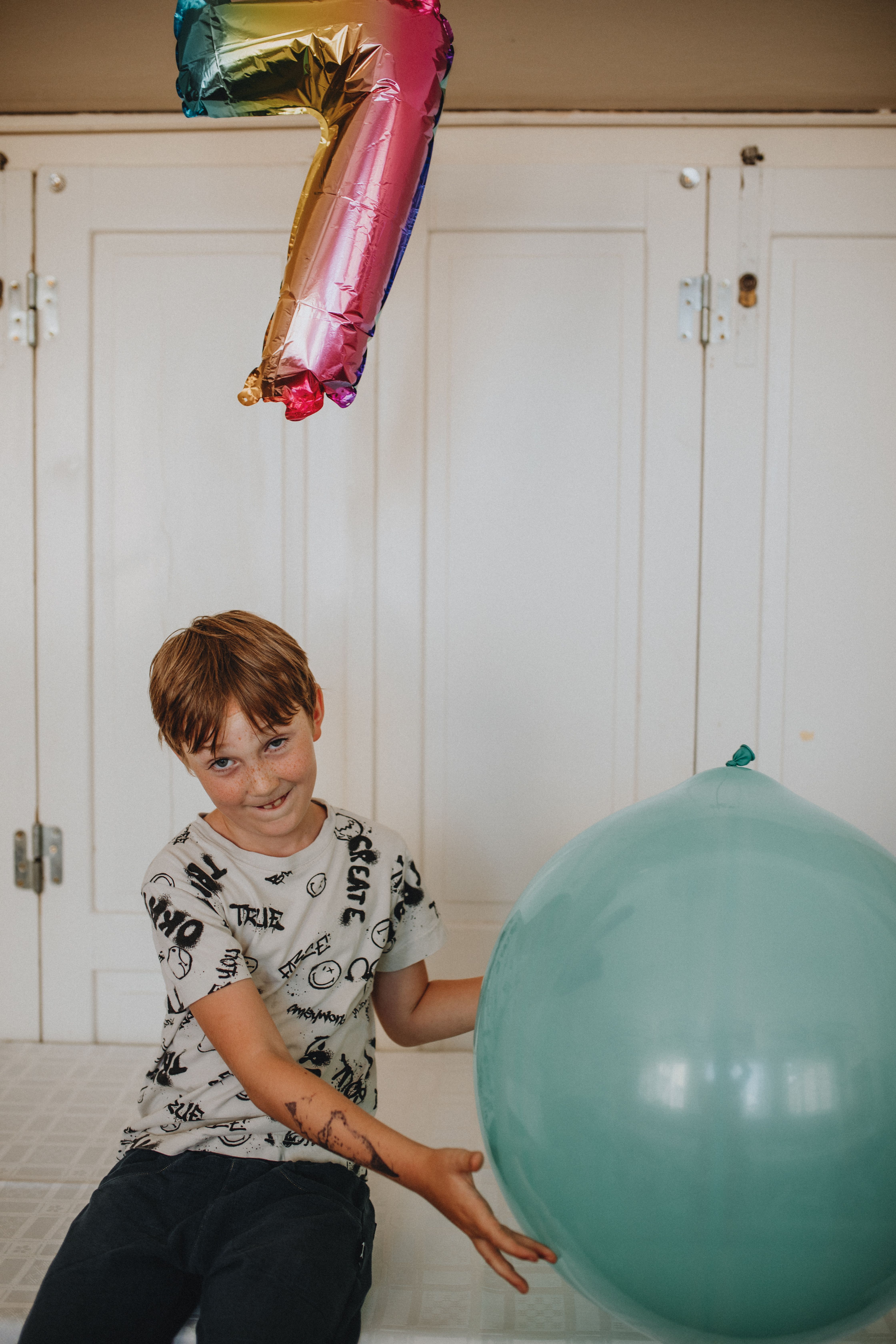 Boy smiling with a colorful number seven balloon indoors.