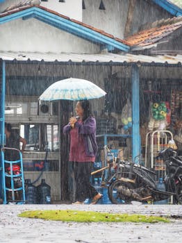 A woman stands under an umbrella during a rainy day on a street in West Java, Indonesia.
