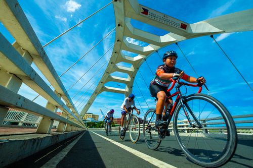 Free Dynamic shot of cyclists racing on a Manila bridge under clear blue skies. Stock Photo