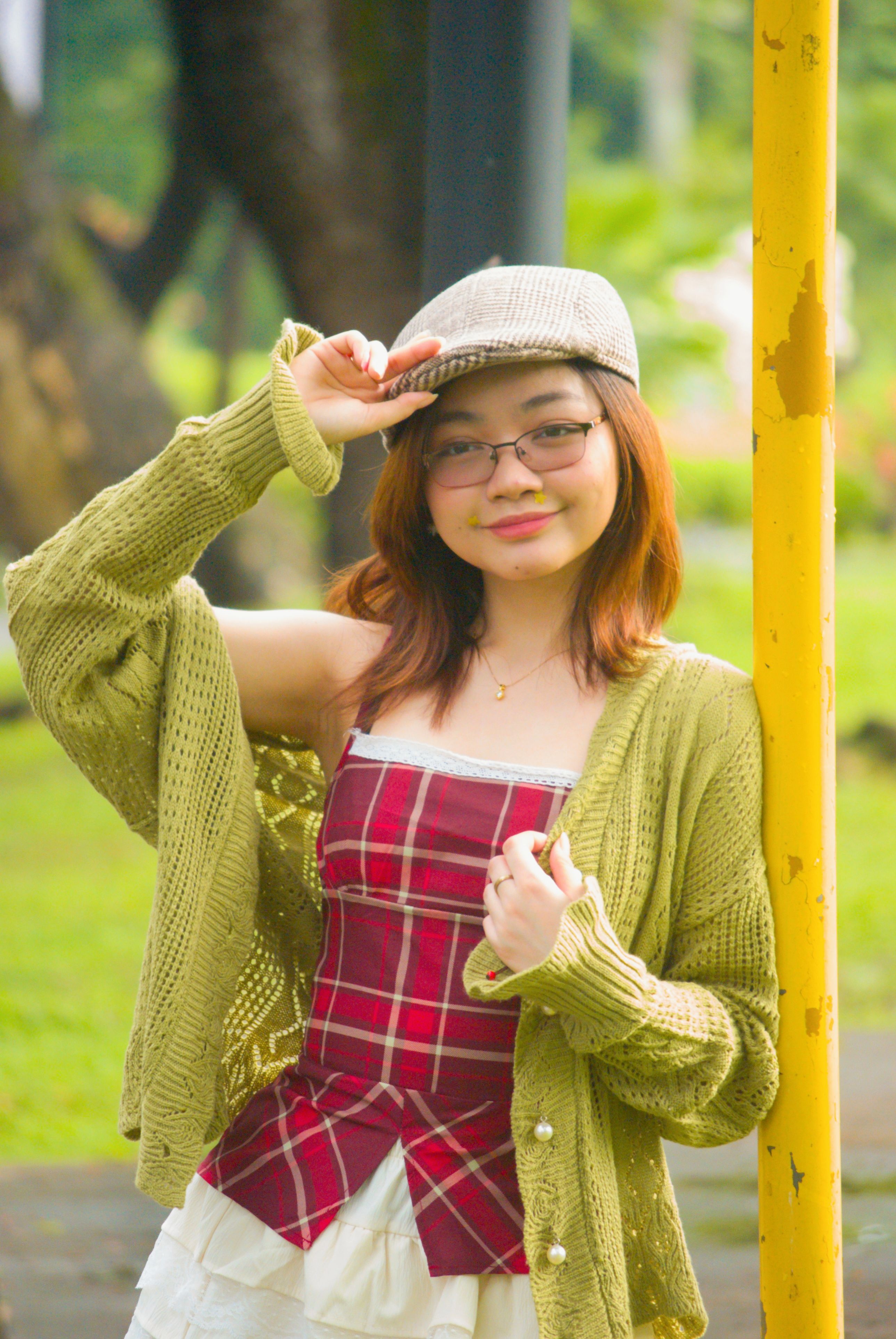 Young woman in vibrant attire and cap posing outdoors in a park setting.