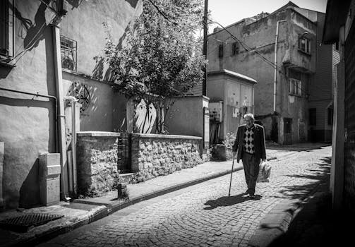 Black and white photo of an elderly man with a cane walking down a cobblestone alley in Istanbul.