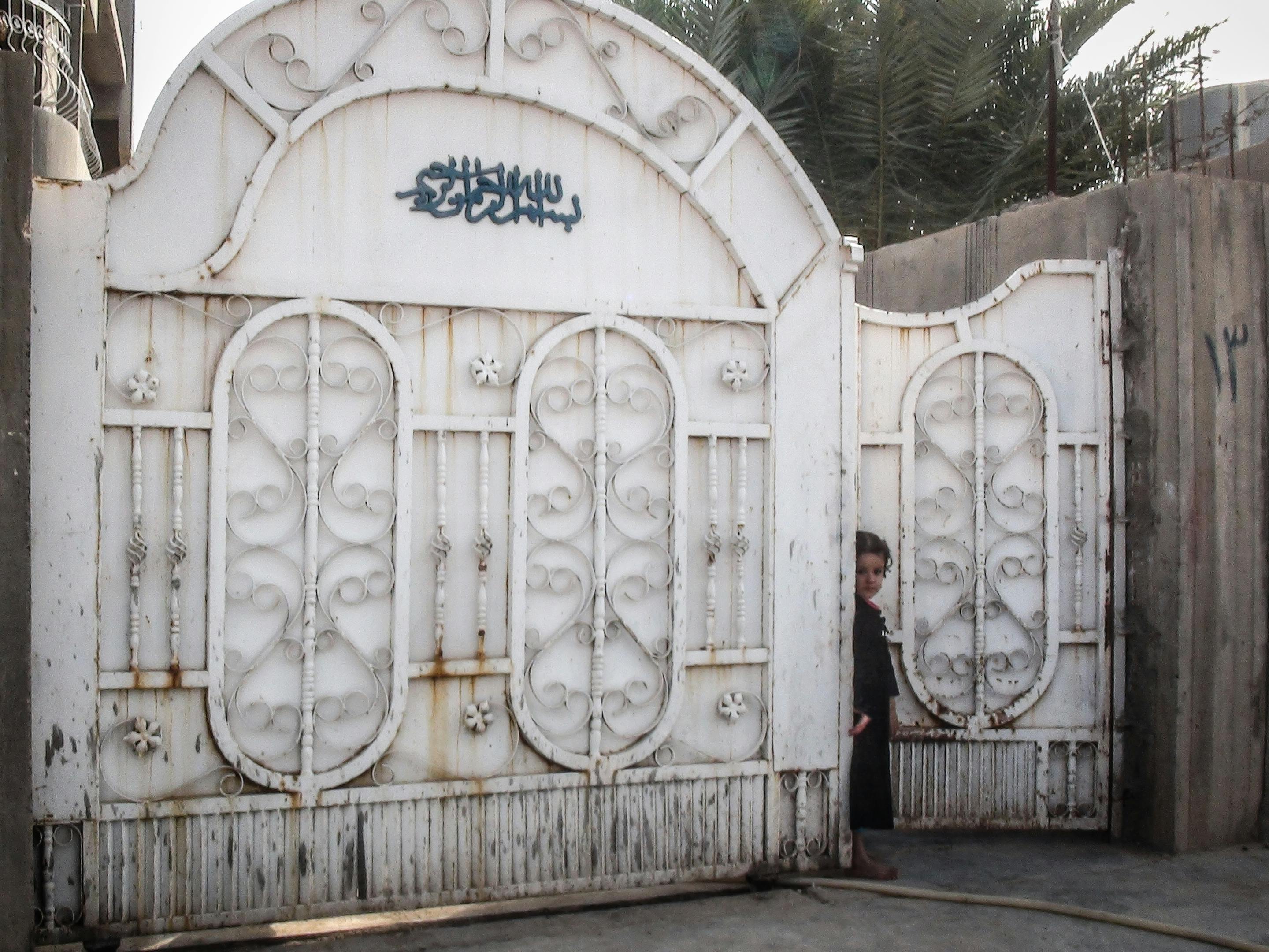 A child peeks from behind a decorative iron gate in Amerli, Iraq, capturing a moment of curiosity and tradition.