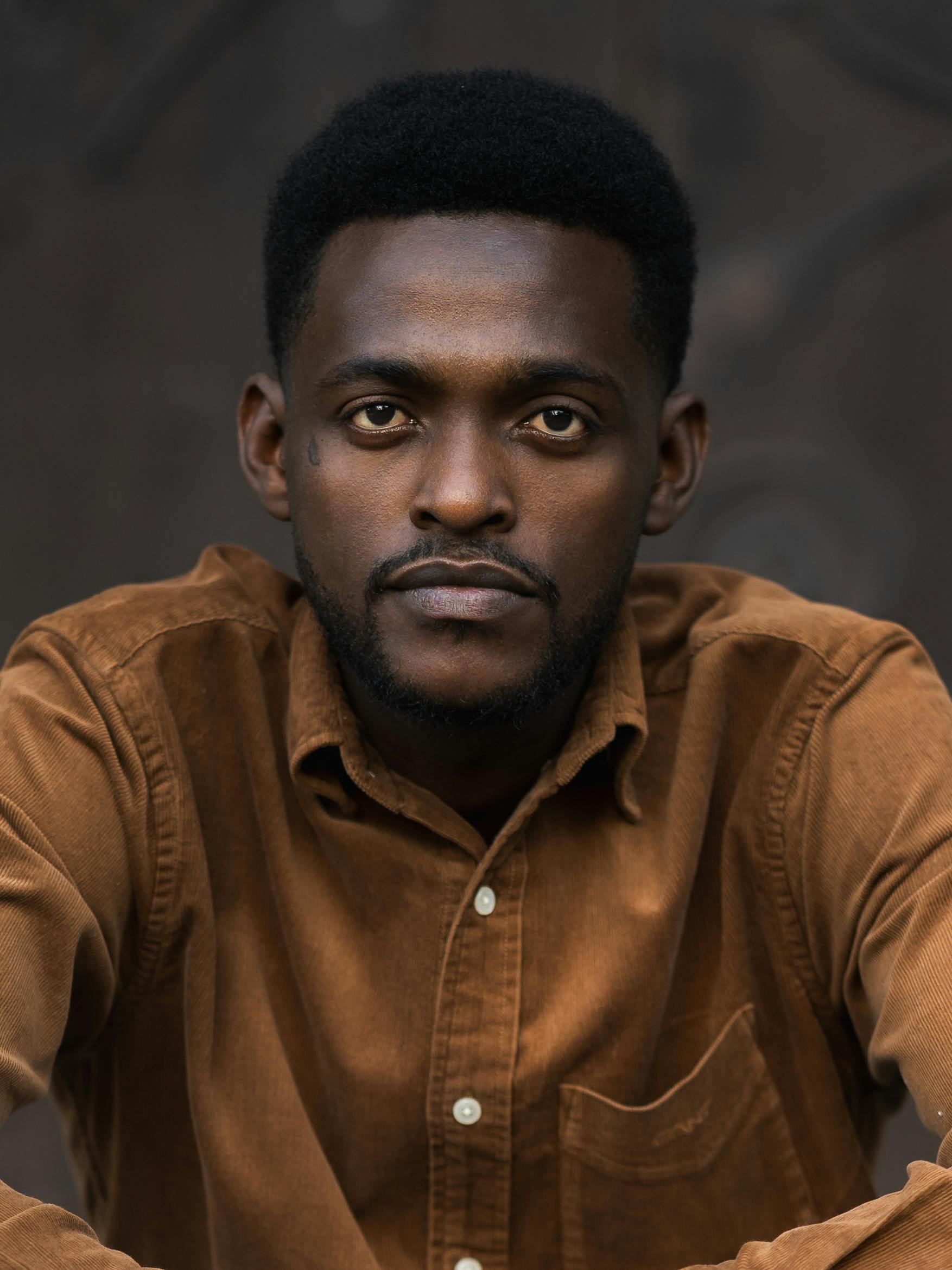Close-up portrait of a man in a brown shirt, featuring a neutral background.