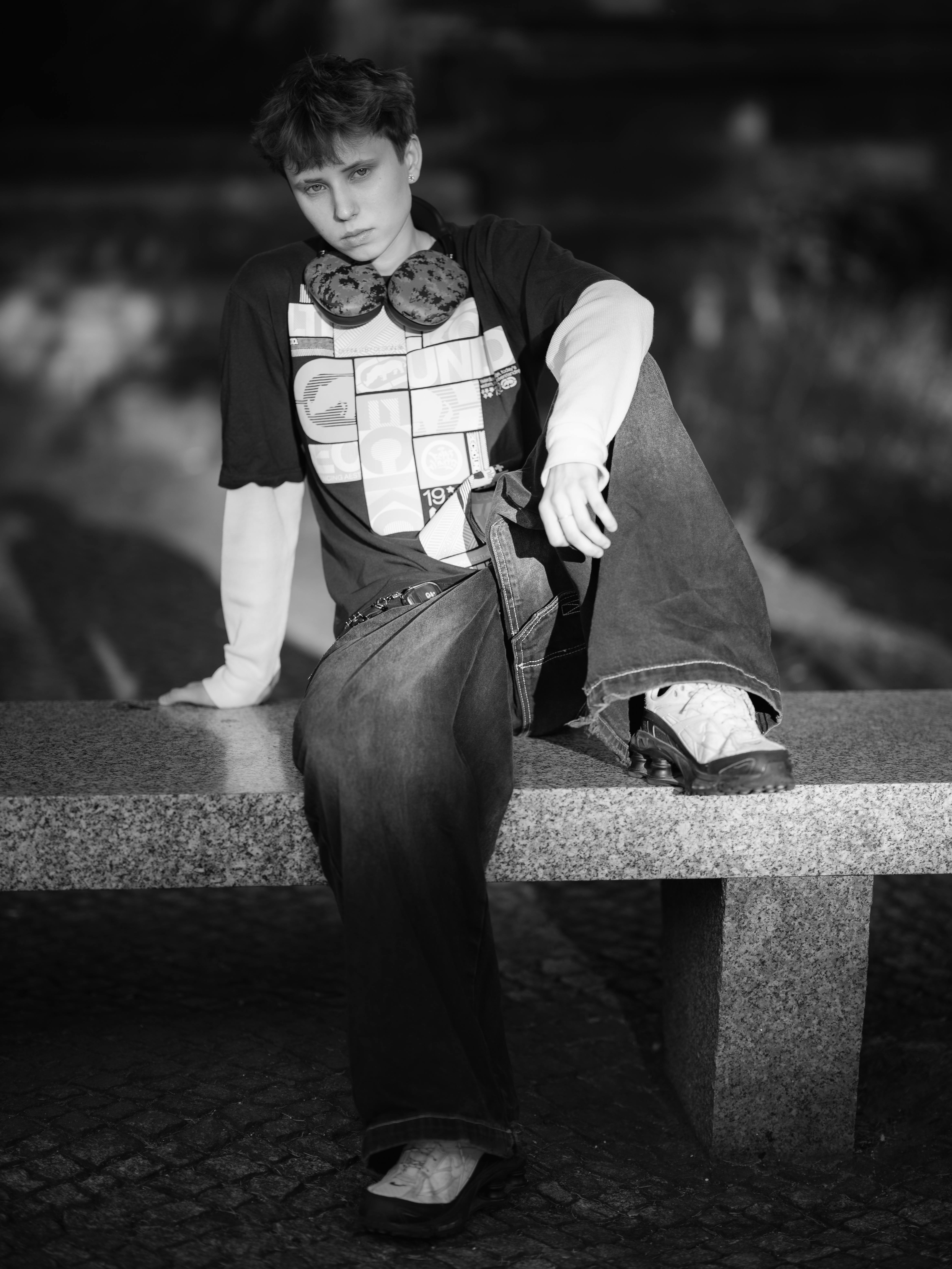 Ücretsiz Gündelik kıyafetler giymiş ve kulaklık takmış bir gencin bankta oturan siyah beyaz portresi. Stok Fotoğraflar