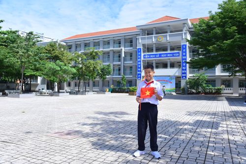 Free Young Vietnamese student holding national flag in bright schoolyard setting. Stock Photo