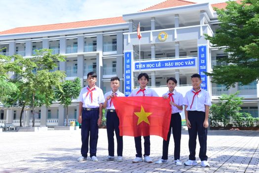 Group of Vietnamese students in school uniform proudly holding national flag in schoolyard.